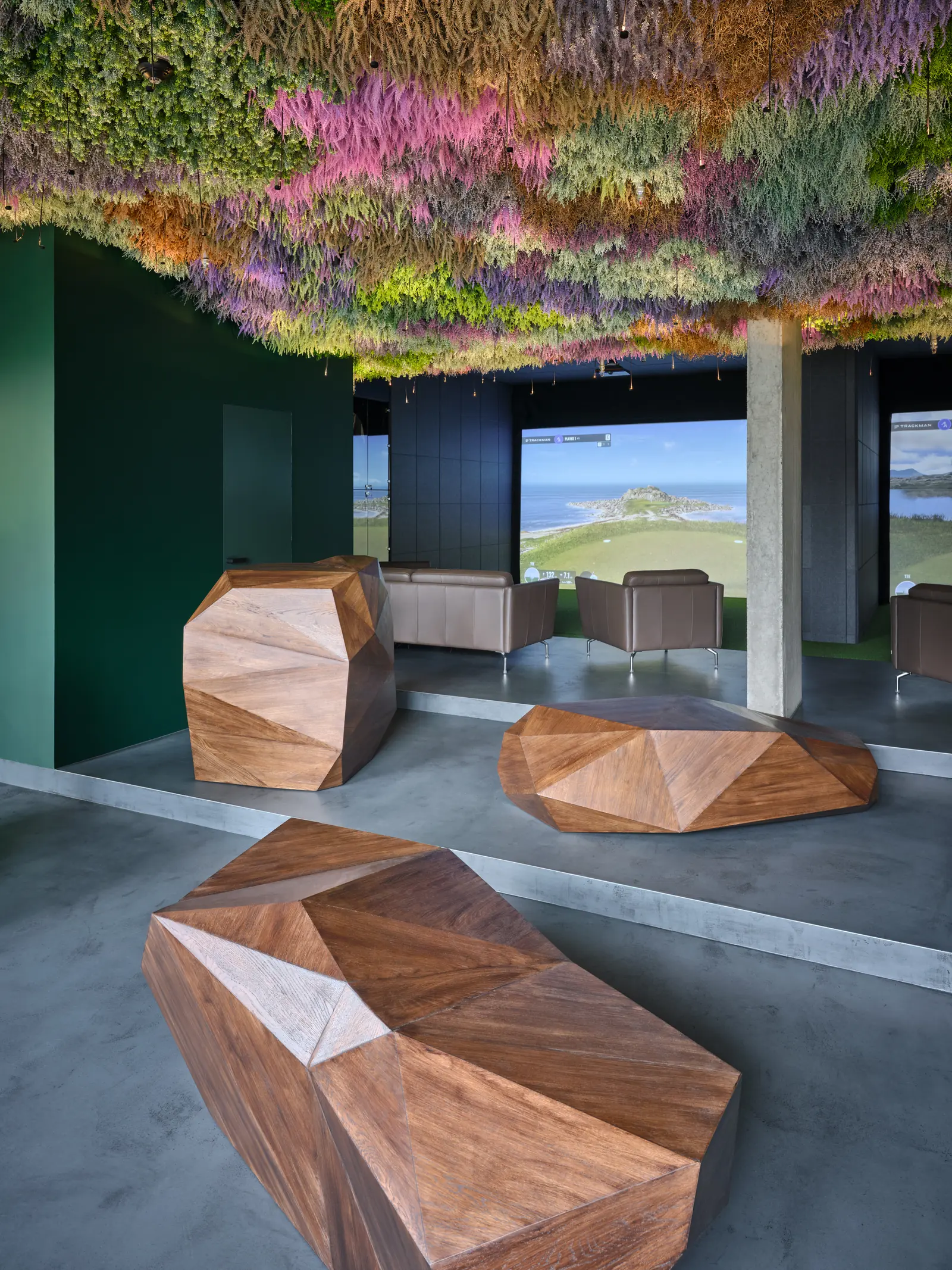 A concrete pillar, wooden tables and a simulator screen under the moss ceiling